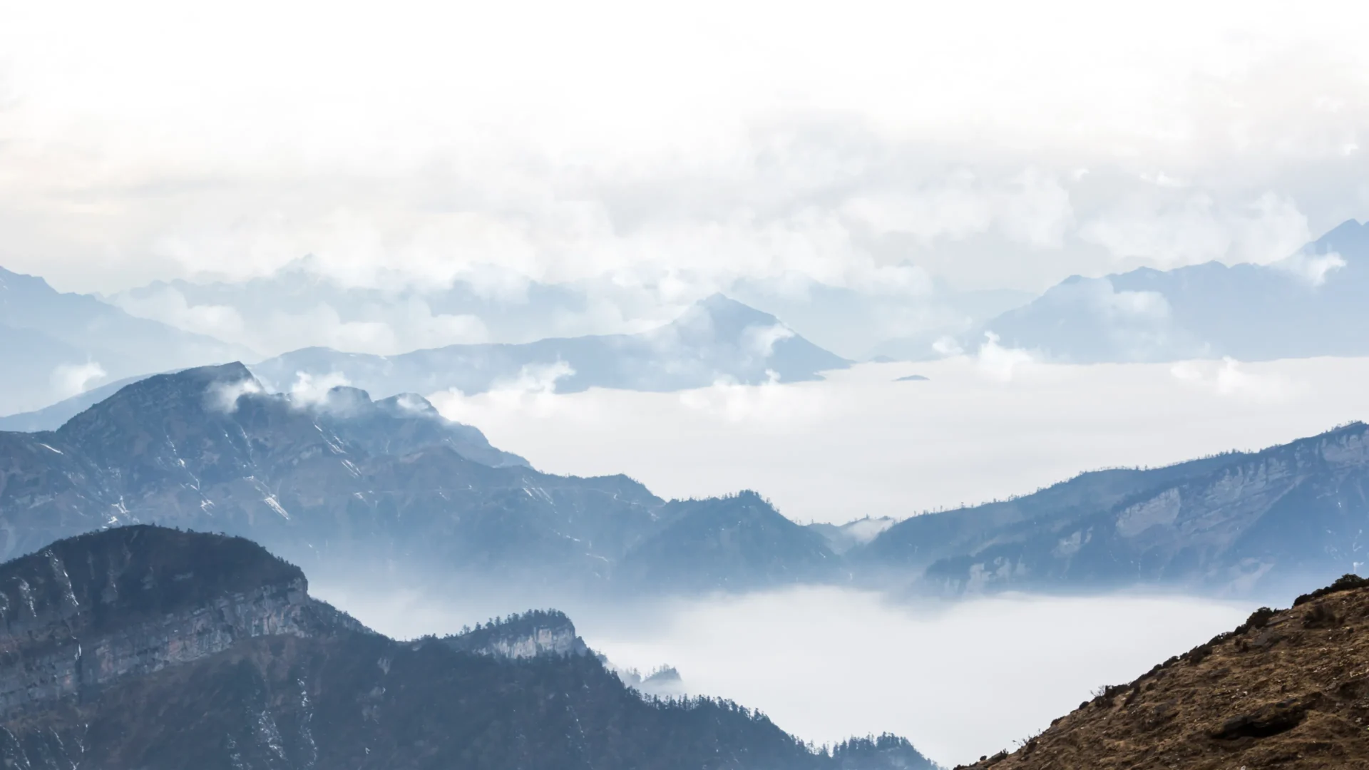 Foggy mountain landscape with layered peaks and soft clouds.