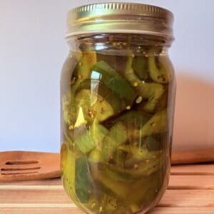 Mason jar of sliced pickles on wooden board